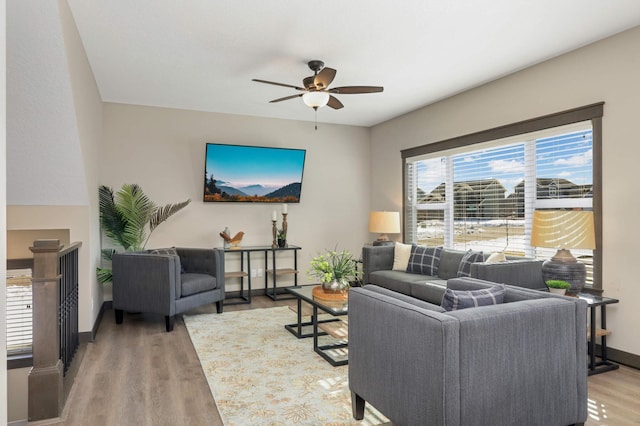 living area with baseboards, light wood-type flooring, and ceiling fan