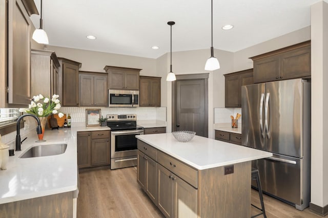 kitchen featuring a kitchen island, light wood-type flooring, light countertops, stainless steel appliances, and a sink