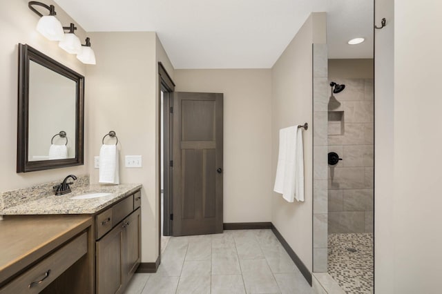 bathroom with vanity, baseboards, tile patterned flooring, and tiled shower