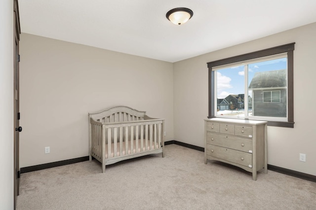 bedroom featuring a crib, baseboards, and light carpet