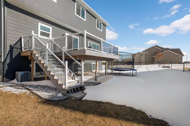 snow covered rear of property with a trampoline, fence, stairway, a wooden deck, and central AC unit