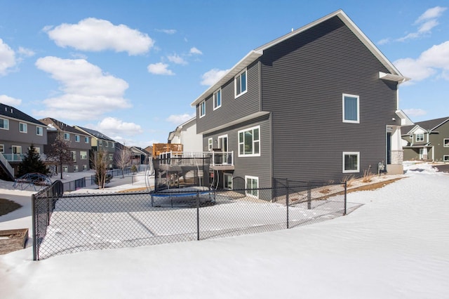 view of snowy exterior with a trampoline, fence, and a residential view