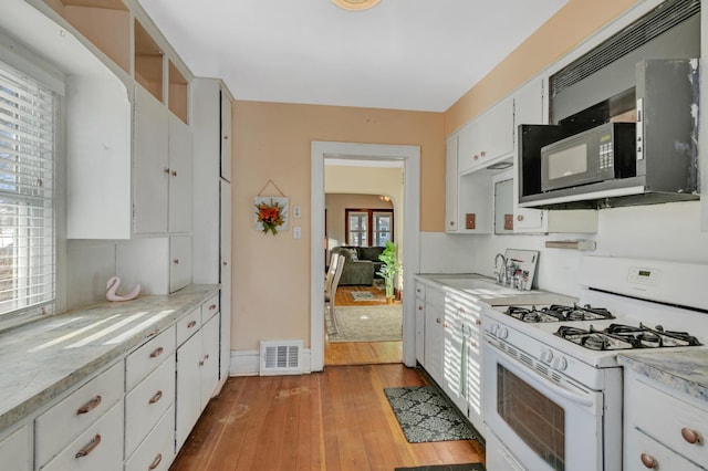 kitchen with black microwave, visible vents, white cabinetry, light countertops, and white gas range oven