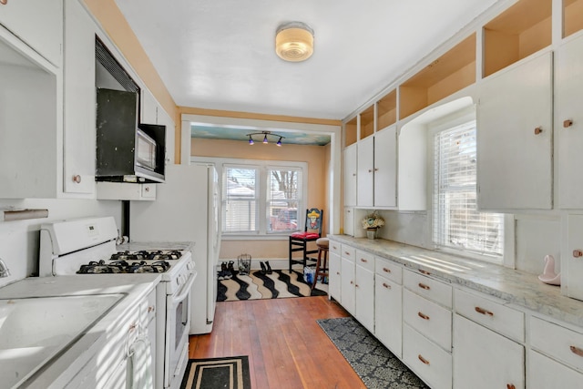 kitchen featuring black microwave, a sink, wood finished floors, white cabinetry, and white gas range