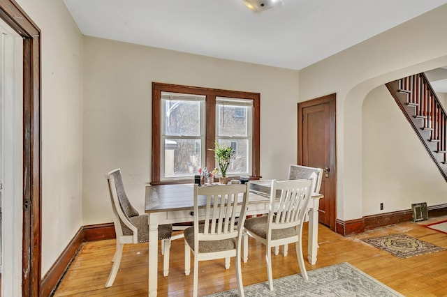 dining room featuring baseboards, stairs, arched walkways, and wood finished floors