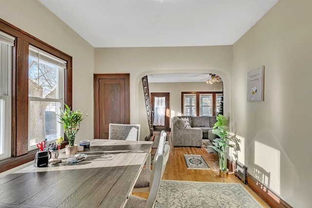 dining space with arched walkways, light wood-type flooring, and a ceiling fan