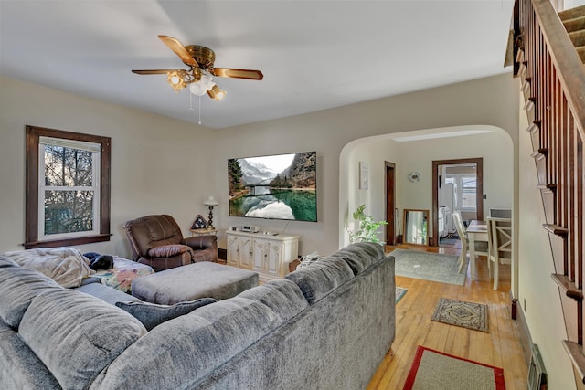 living room with a ceiling fan, arched walkways, and light wood finished floors