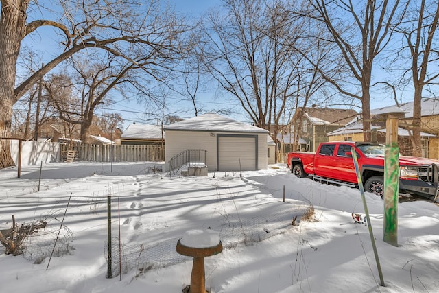 yard covered in snow with an outbuilding, a detached garage, and fence