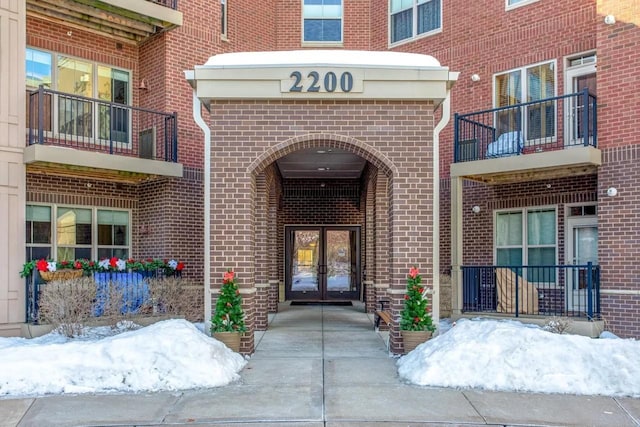 snow covered property entrance featuring brick siding and french doors