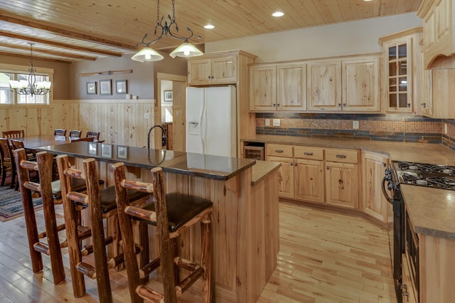 kitchen with white refrigerator with ice dispenser, decorative light fixtures, and a center island with sink