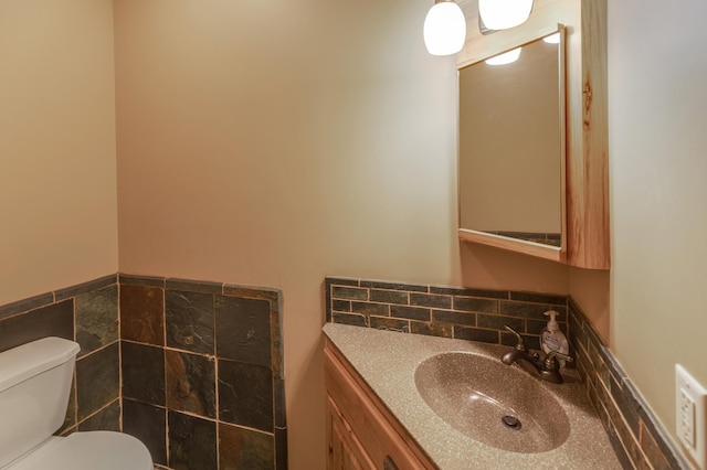 half bathroom with a wainscoted wall, vanity, toilet, and tile walls