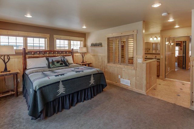 carpeted bedroom with wooden walls, visible vents, wainscoting, ensuite bathroom, and recessed lighting