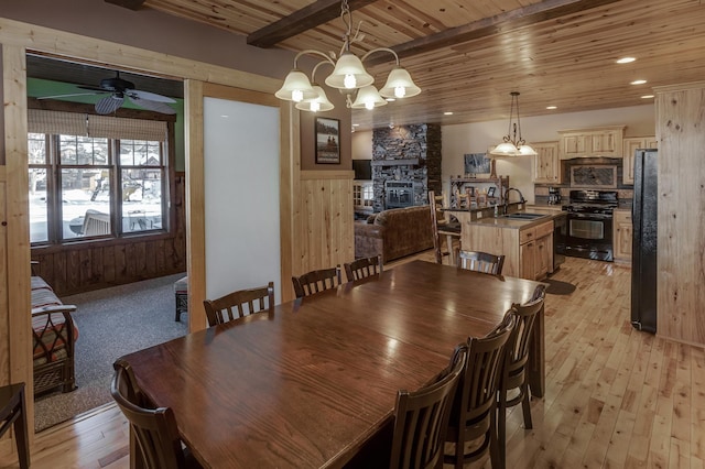 dining area featuring light wood finished floors, recessed lighting, wood ceiling, a stone fireplace, and beamed ceiling