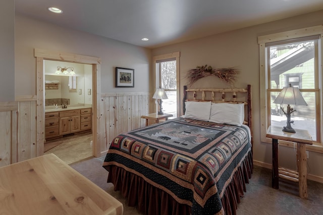 bedroom with light carpet, a wainscoted wall, ensuite bathroom, a sink, and recessed lighting