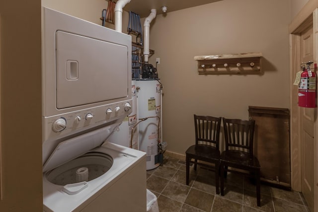 washroom with gas water heater, laundry area, dark tile patterned floors, baseboards, and stacked washer / drying machine