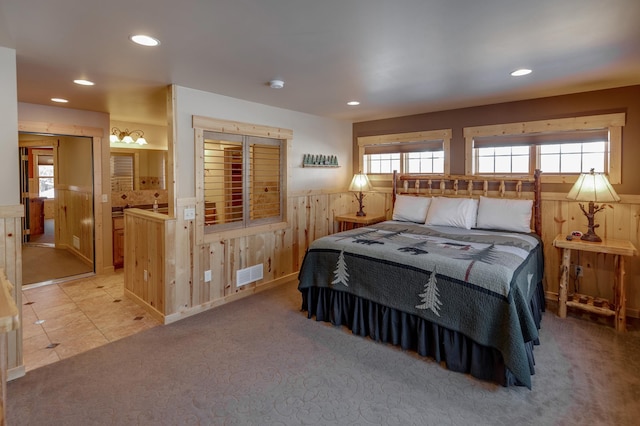 bedroom featuring wood walls, visible vents, light colored carpet, and wainscoting