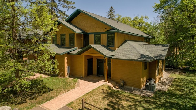 view of front facade with central air condition unit, a shingled roof, and a front yard