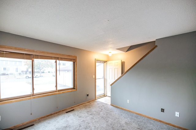 empty room with a textured ceiling, light carpet, visible vents, baseboards, and stairway