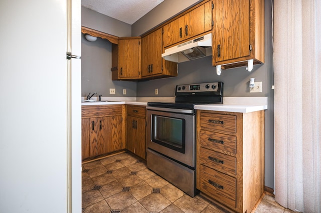 kitchen featuring brown cabinetry, freestanding refrigerator, stainless steel electric range, light countertops, and under cabinet range hood