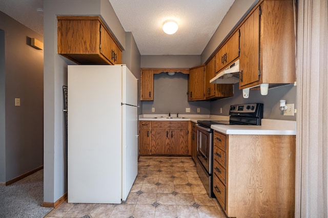 kitchen with under cabinet range hood, light countertops, freestanding refrigerator, stainless steel electric stove, and brown cabinetry