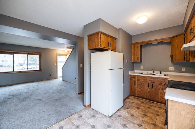 kitchen featuring light countertops, a sink, freestanding refrigerator, and brown cabinets