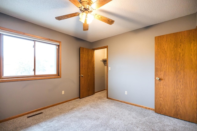 unfurnished room with ceiling fan, a textured ceiling, light carpet, visible vents, and baseboards