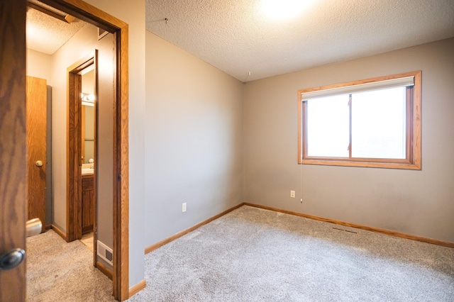 empty room with light colored carpet, a textured ceiling, and baseboards