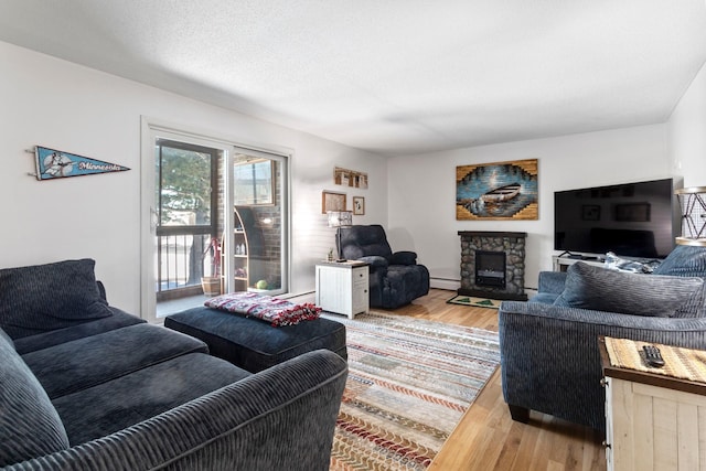 living room with a fireplace, light wood-style flooring, baseboard heating, and a textured ceiling