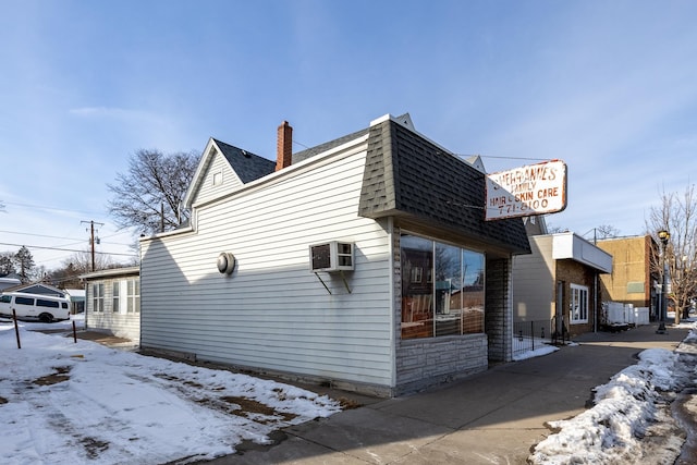 snow covered property featuring a shingled roof, a chimney, and a wall mounted AC