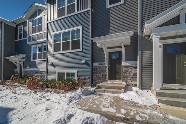 snow covered property entrance with stone siding