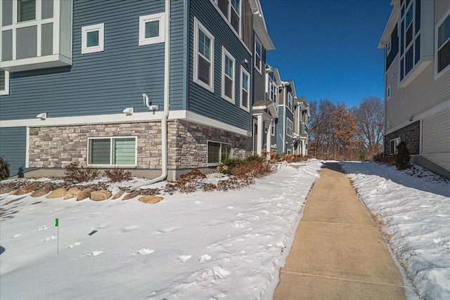 snow covered property featuring a residential view and stone siding