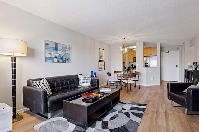 living room with an inviting chandelier, baseboards, light wood-type flooring, and a textured ceiling