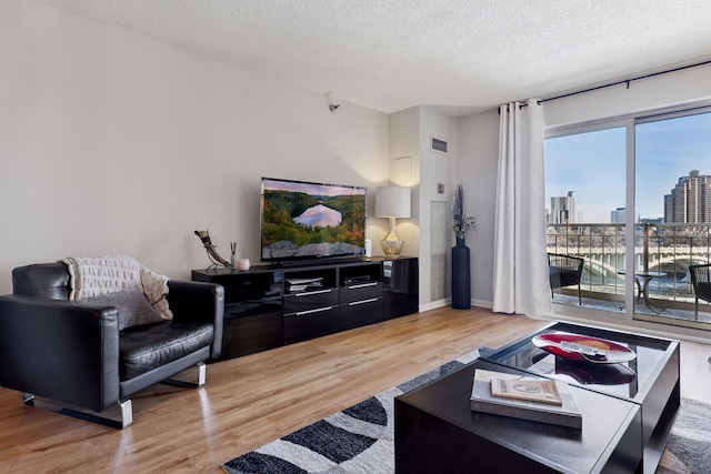 living room featuring visible vents, baseboards, a textured ceiling, and light wood-style flooring