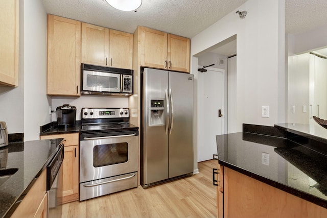 kitchen featuring dark stone countertops, light wood-style flooring, light brown cabinetry, and stainless steel appliances