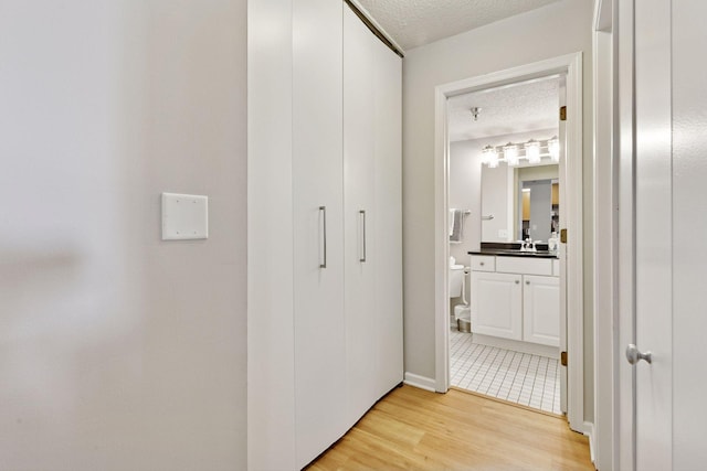 hall featuring a sink, light wood-style floors, and a textured ceiling