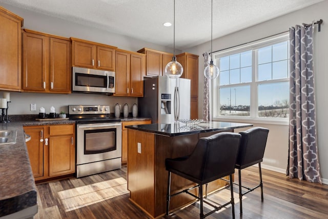 kitchen featuring dark countertops, dark wood-style floors, appliances with stainless steel finishes, a center island, and hanging light fixtures