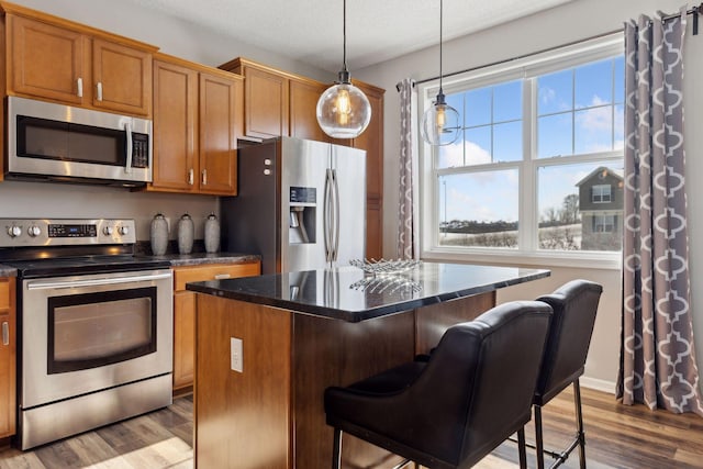 kitchen featuring a center island, stainless steel appliances, hanging light fixtures, a textured ceiling, and wood finished floors