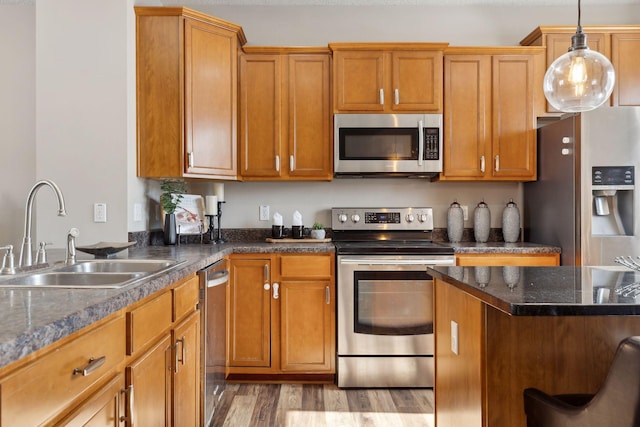 kitchen featuring light wood finished floors, brown cabinetry, decorative light fixtures, stainless steel appliances, and a sink