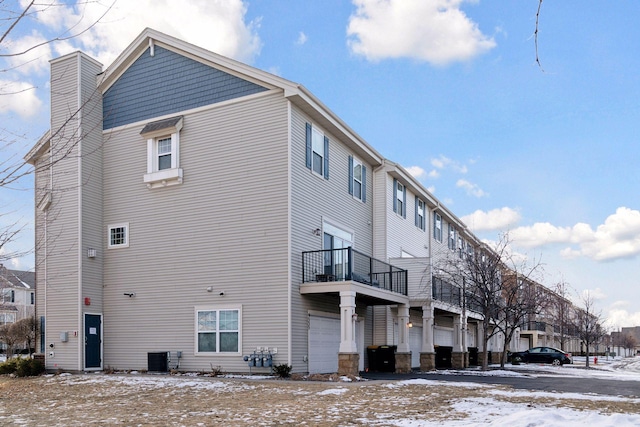 view of snowy exterior with a garage, a chimney, a balcony, and central air condition unit