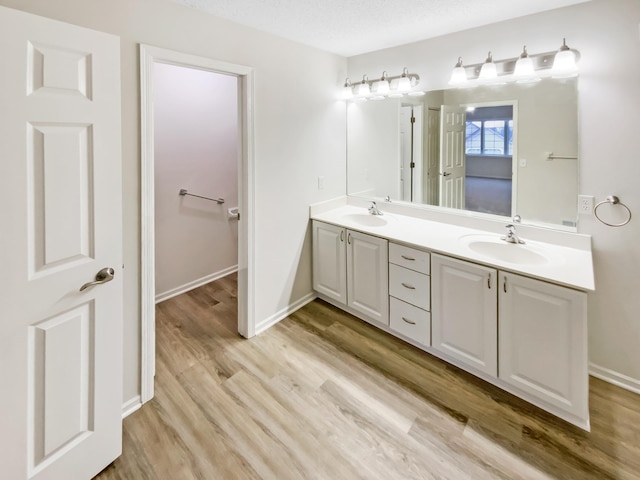 bathroom with double vanity, baseboards, a sink, and wood finished floors