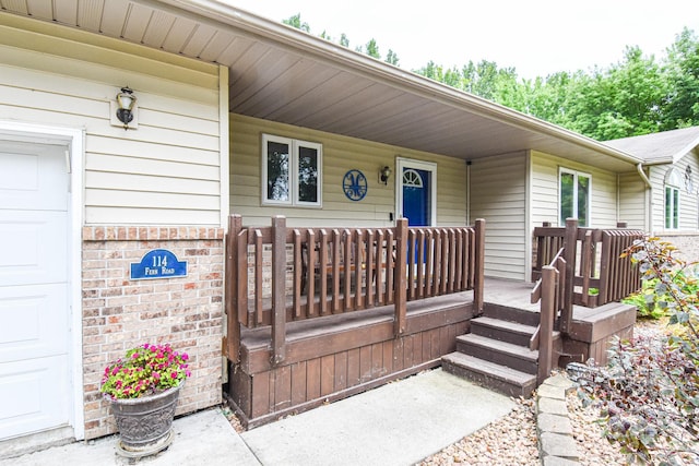 view of exterior entry with a garage, brick siding, and a porch