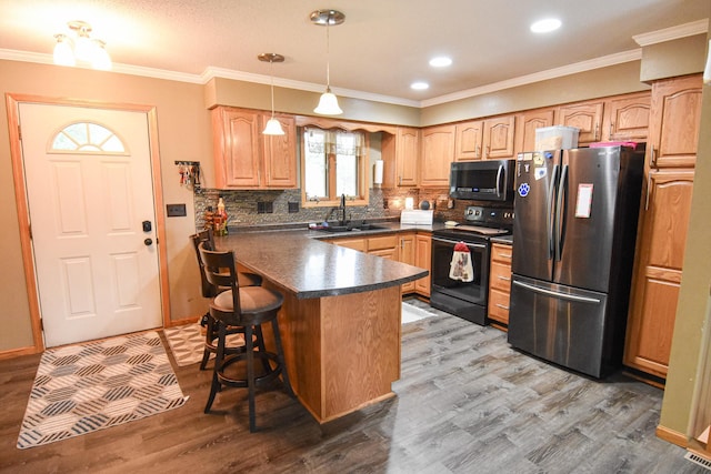 kitchen featuring a breakfast bar, a sink, appliances with stainless steel finishes, dark countertops, and pendant lighting