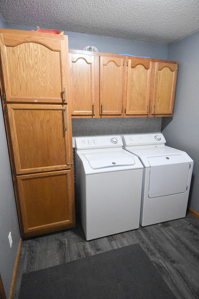 clothes washing area featuring washing machine and clothes dryer, cabinet space, dark wood-type flooring, a textured ceiling, and baseboards