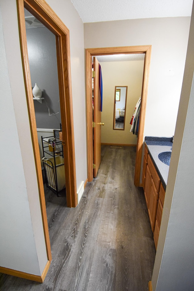 hallway featuring dark wood-style floors, a sink, and baseboards