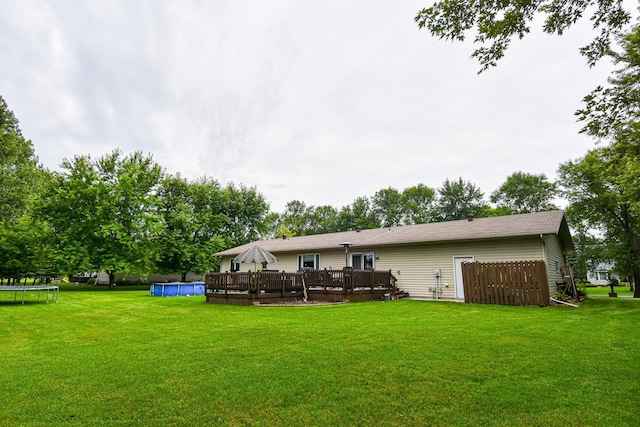 back of property featuring a deck, a trampoline, a lawn, and an outdoor pool