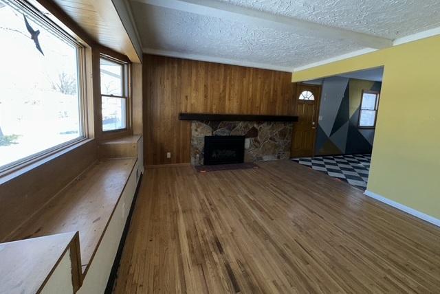 unfurnished living room featuring wood walls, a stone fireplace, a textured ceiling, wood finished floors, and baseboards