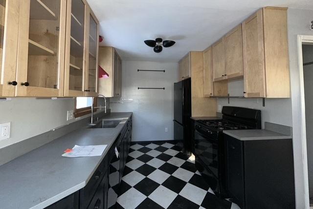 kitchen featuring dark floors, glass insert cabinets, light brown cabinetry, black appliances, and a sink