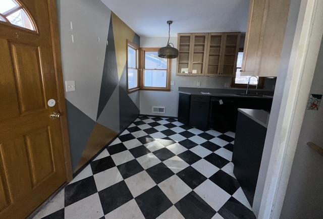 kitchen with light floors, visible vents, hanging light fixtures, glass insert cabinets, and a sink