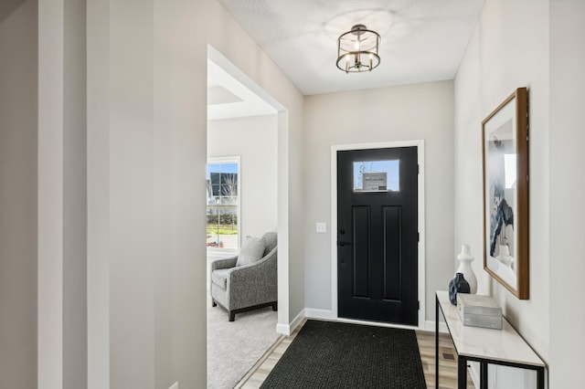 entryway featuring light wood finished floors, baseboards, and an inviting chandelier