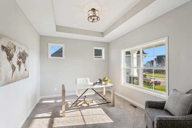 office area featuring light colored carpet, a tray ceiling, visible vents, and baseboards